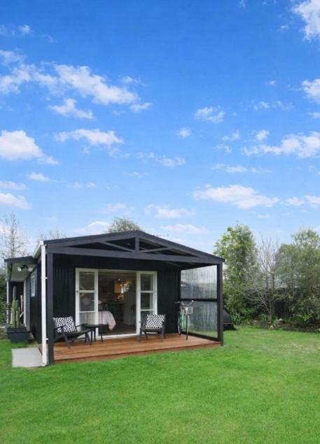 a black house with a deck in a field of grass at Mangapiko Cabin in Pirongia