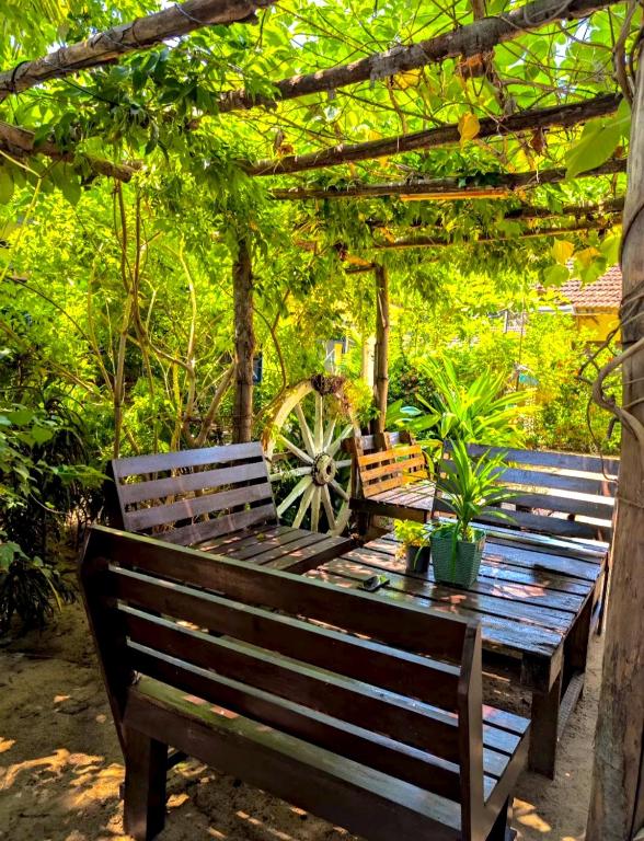 two wooden benches sitting under a pergola with a wheel at Eastwind Surf Camp - Surf & Stay in Arugam Bay