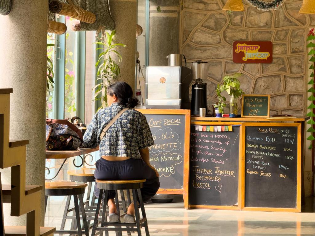 a woman sitting on a stool in front of a bar at Jaipur Jantar Hostel in Jaipur