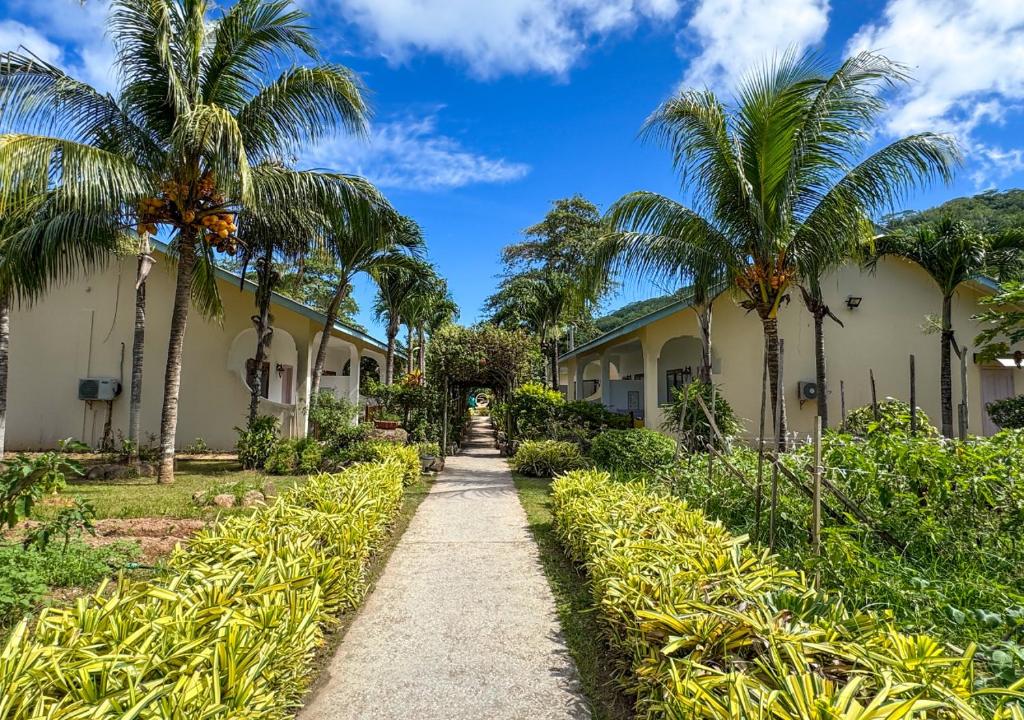 a path through the courtyard of a resort with palm trees at Coral Apartments in La Digue