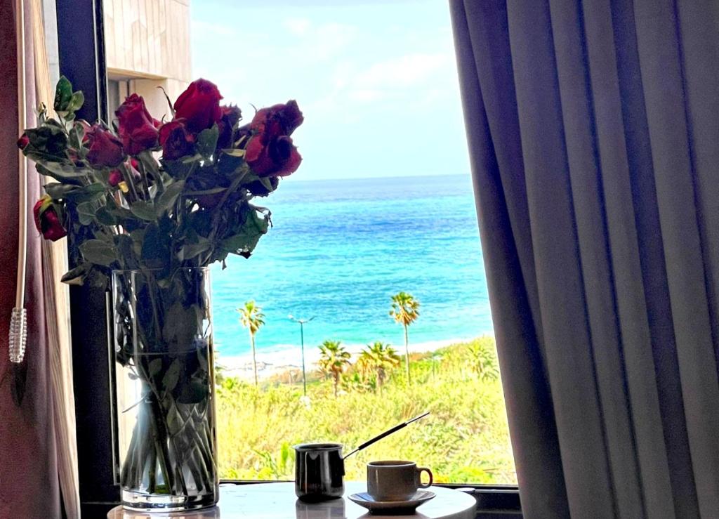 a vase of flowers on a window sill with the ocean at Rawsheh Boutique Hotel in Beirut
