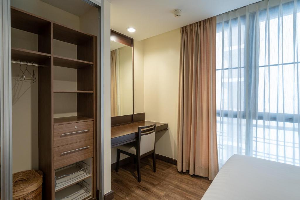A compact bedroom workspace beside an open wardrobe and curtained window.