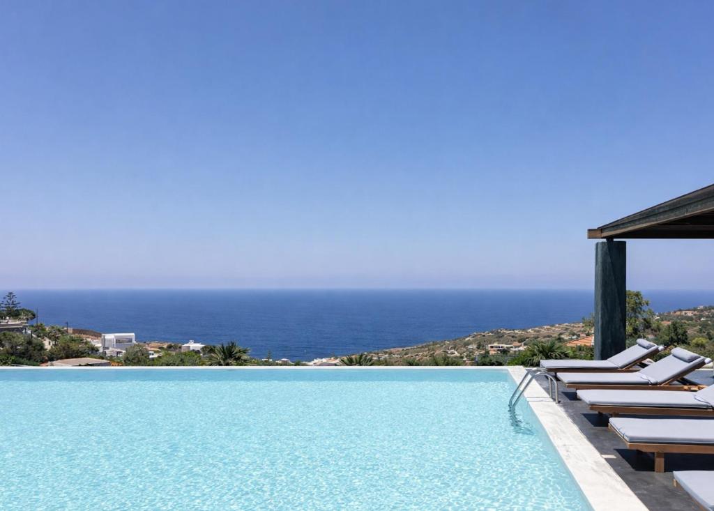 a pool with chairs and the ocean in the background at Villa Dei Sogni, for the Design Lovers,By ThinkVilla in Agia Pelagia