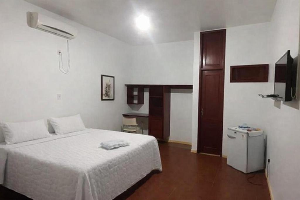 a bedroom with a white bed and a small refrigerator at Garden Hotel e Eventos in Benevides