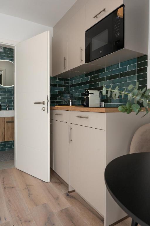 a kitchen with white cabinets and a black tile wall at BLI One in Vilsbiburg