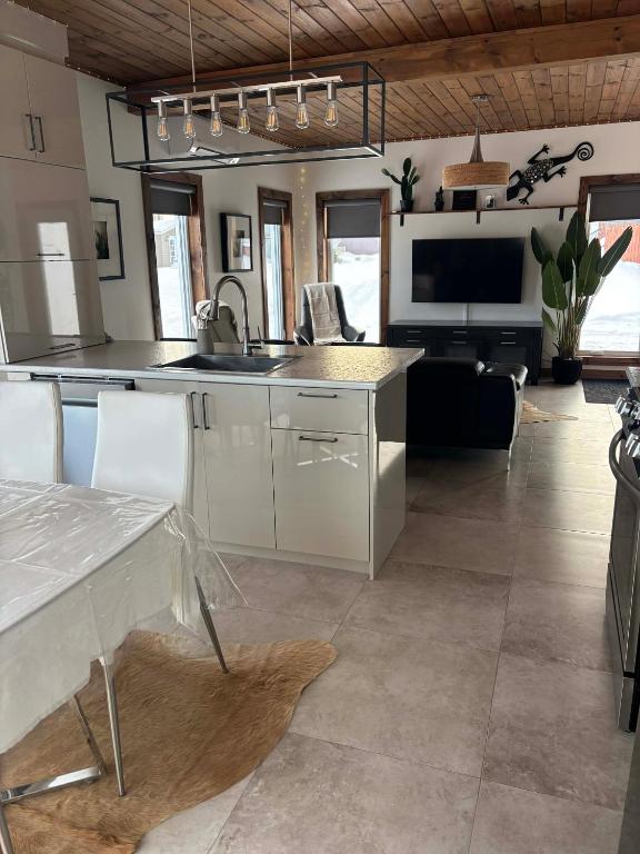 eine Küche mit weißen Schränken, einem Tisch und einem Fernseher in der Unterkunft Les Chalets Baie Cascouia in Larouche