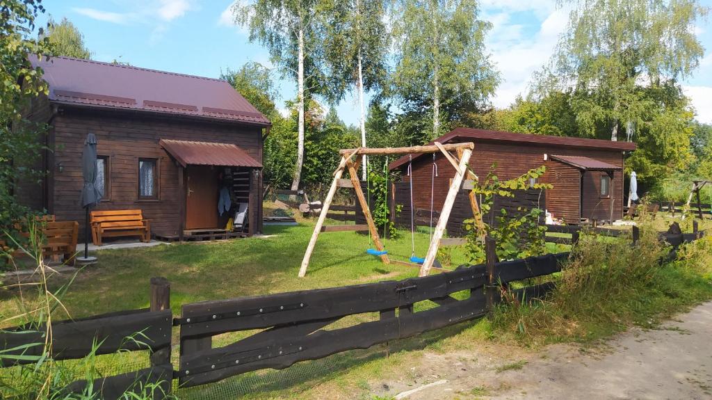 a log cabin with a swing and a house at Domki nad Wałpuszem in Stare Kiejkuty