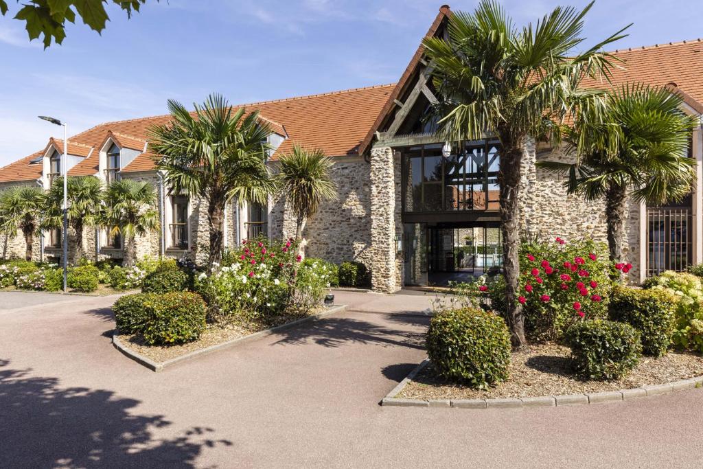a building with palm trees and flowers in front of it at Hotel Les Suites - Domaine de Crécy in Crécy-la-Chapelle