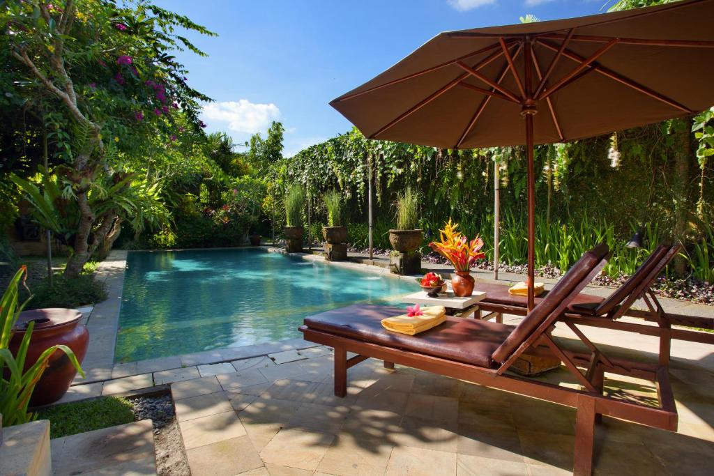 an umbrella and a bench next to a swimming pool at Barong Resort and Spa in Ubud