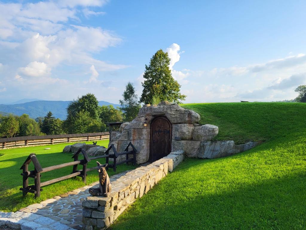 a stone building with a gate in a field at Domek Hobbita z jaskinią SPA - Osada Jaworzyny in Tokarnia