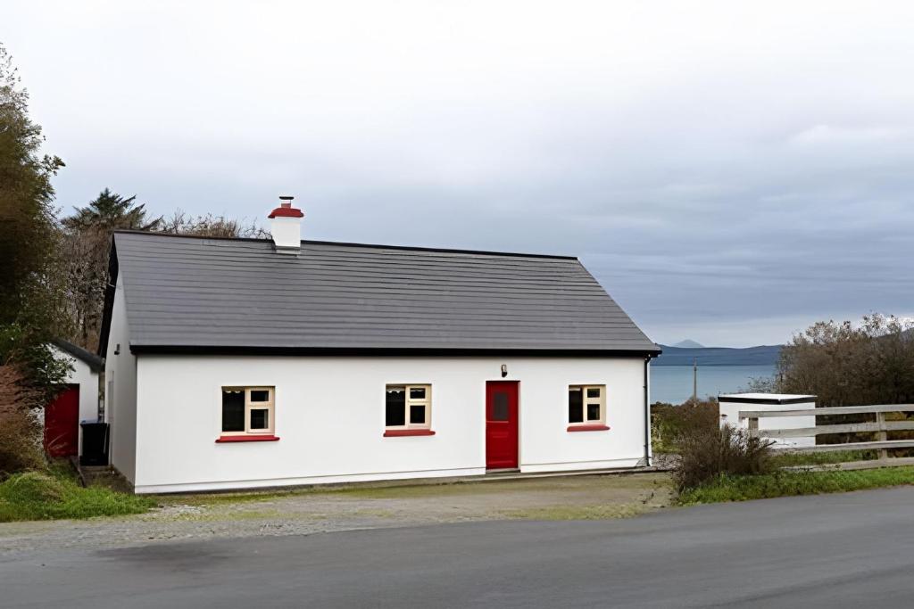 a white house with a red door on the side of a road at Nancy's Seaside Cottage, Renvyle in Renvyle