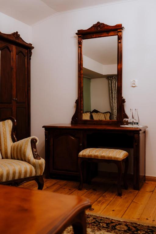 Antique wooden vanity with tall mirror, cushioned stool, striped armchair, bottled water on tabletop.