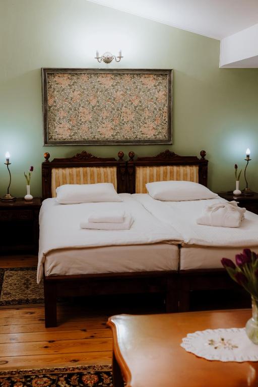 Bedroom with green accent wall, two single beds with folded towels, evening lamps and flowers.