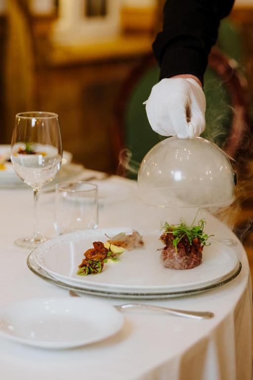 White-gloved hand lifting glass cloche to reveal smoky plated dish at fine dining table.