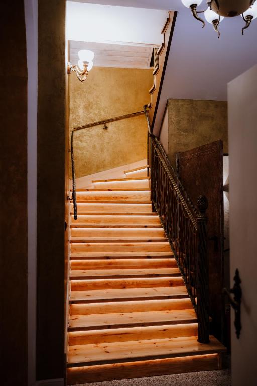 Warm wooden staircase with under-step lighting and ornate iron railing in narrow hallway.