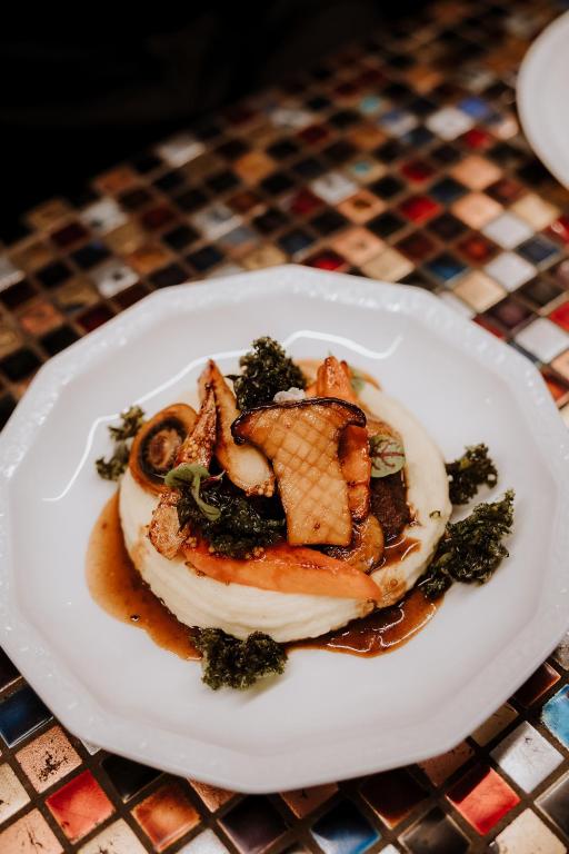 Mashed potato ring topped with sautéed mushrooms and greens, glossy brown sauce drizzled.