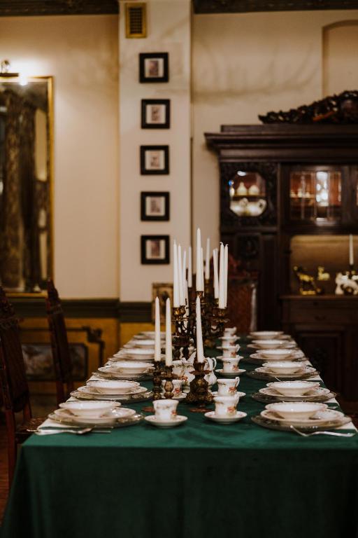 Long banquet table set with china, multiple candelabras and tall white candles in dim dining room.