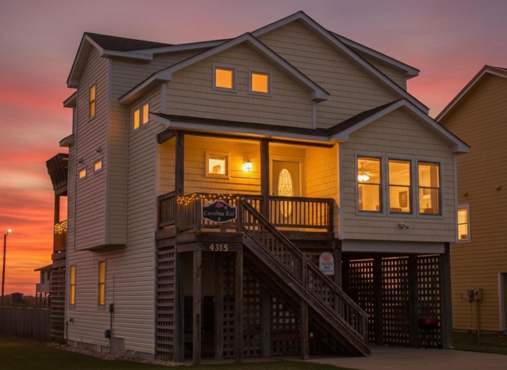 a house with a staircase in front of a sunset at Carolina Kai II - Kitty Hawk MP 3, 228 Yards to Beach, Ocean View, Pool, Hot Tub in Kitty Hawk