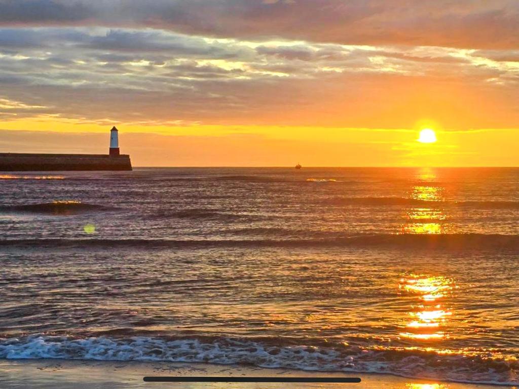 a lighthouse on a beach with the sun setting at Sunrise Cottage in Berwick-Upon-Tweed