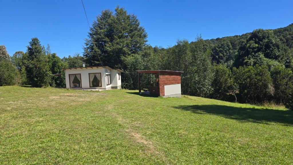 a small building on a grassy field with a house at Casa de campo in Lago Ranco
