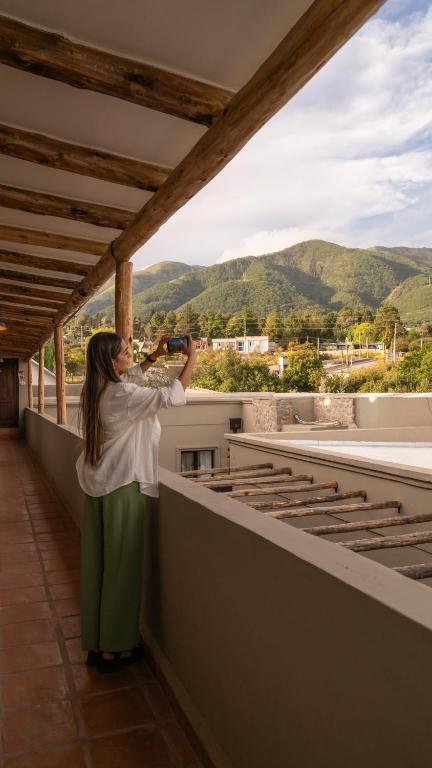 a woman taking a picture of the mountains from a balcony at Hotel Boutique con Desayuno in Tafí del Valle