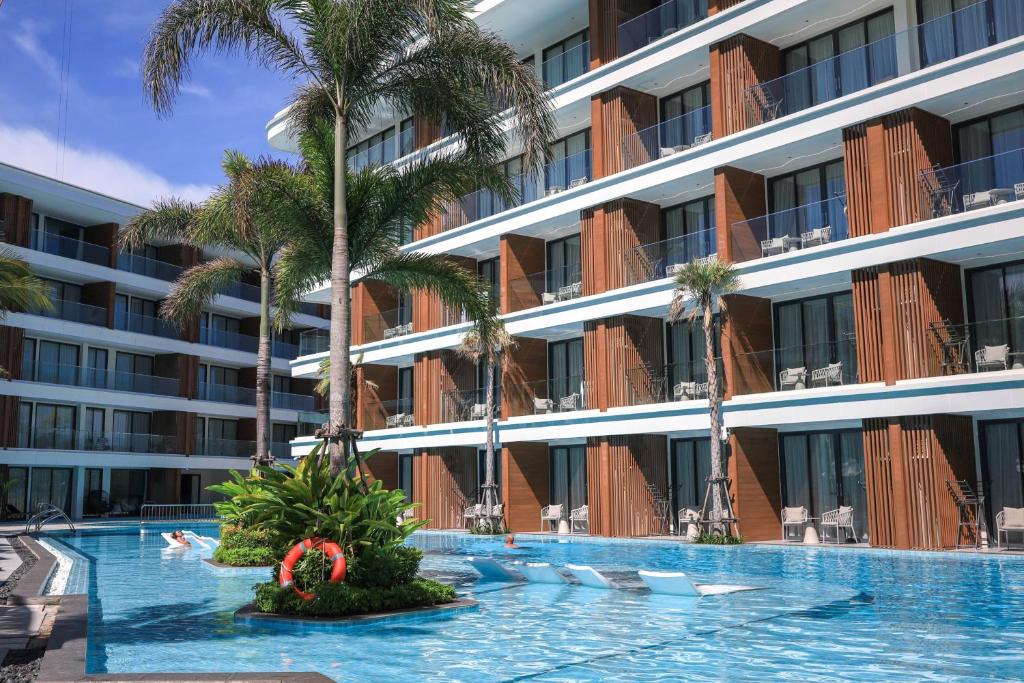 a swimming pool in front of a building with palm trees at The Sunshine Beach Resort Studio in Layan Beach
