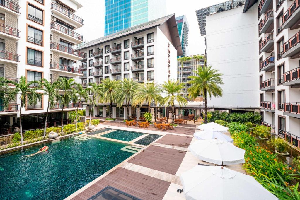 A palm-lined outdoor pool courtyard with loungers, umbrellas and surrounding buildings.