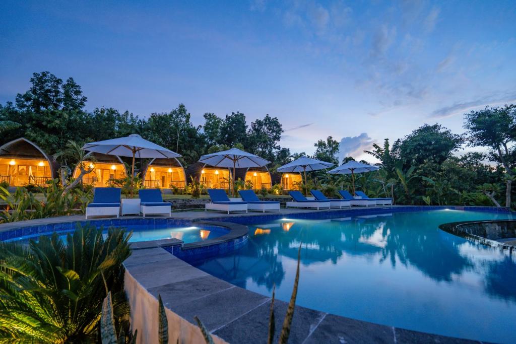 a resort pool with chairs and umbrellas at night at Ratna's Green Hill Penida by Bali Cabin in Nusa Penida