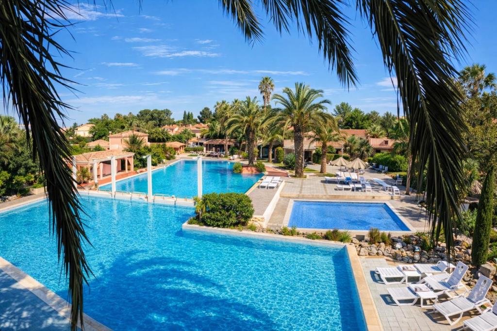 a pool at a resort with palm trees at Studio cabine climatise Malibu Village in Canet-en-Roussillon