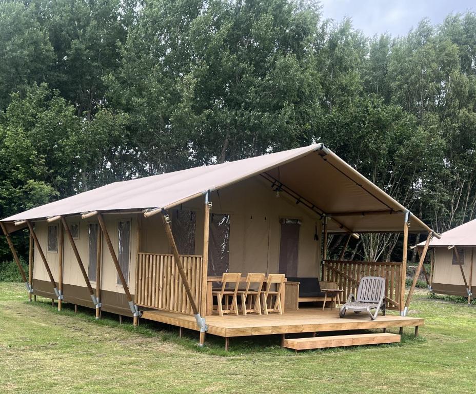 a tent with a deck and chairs in a field at Glampingtent Serengeti in Zwartemeer