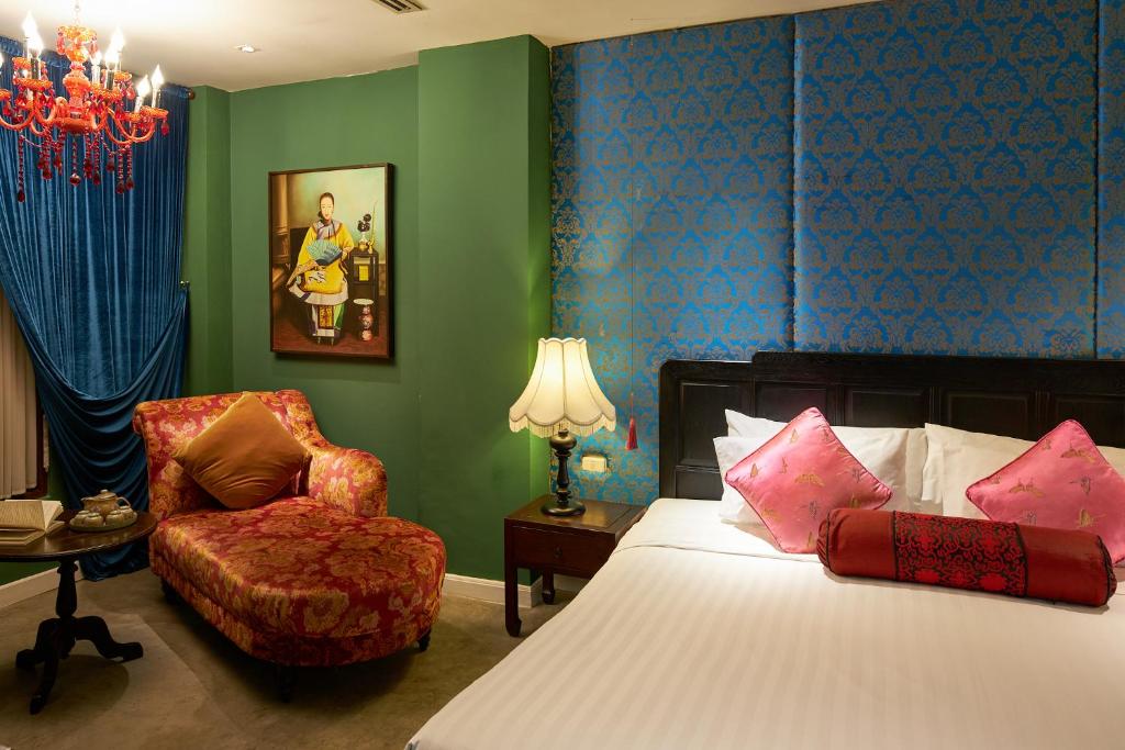 A colourful room with a bed, patterned chaise longue and chandelier.