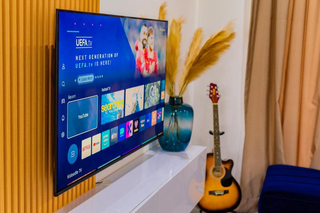 a flat screen tv sitting on a shelf with two guitars at 7th Heaven Apartments in Gaborone