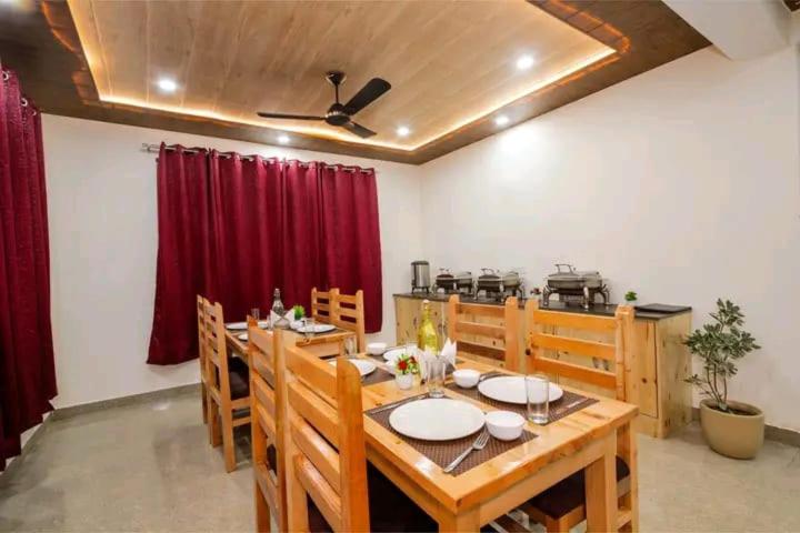 a dining room with a wooden table and red curtains at Pinnacle view in Manāli