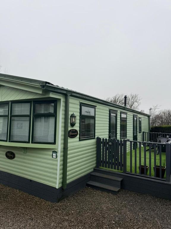 a green trailer with a porch and a fence at The West Lakes Caravan in Lamplugh