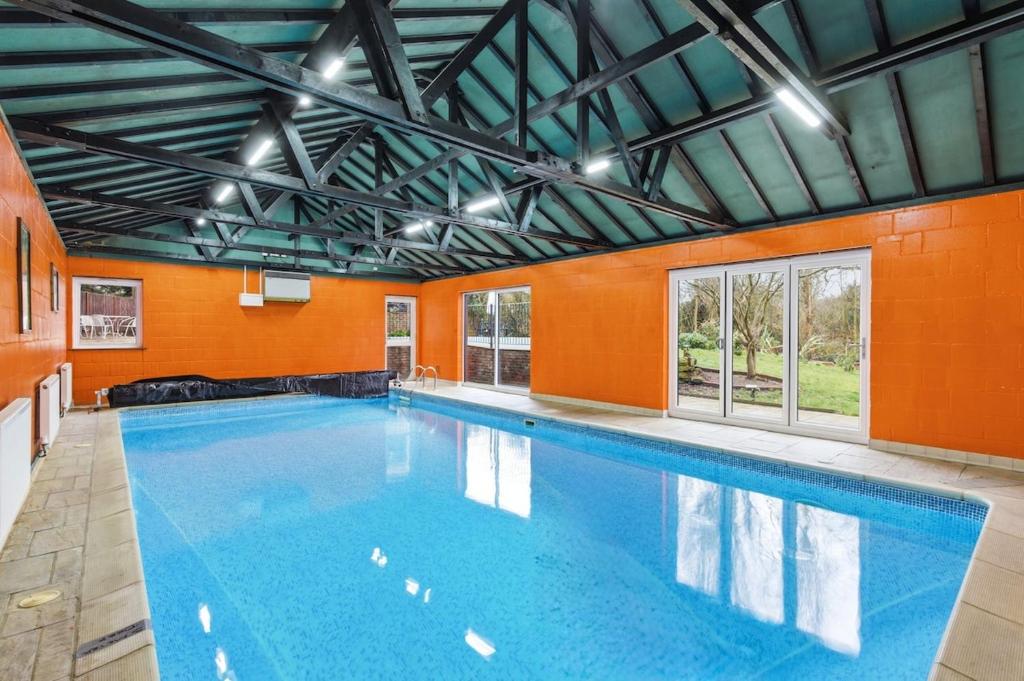 a large swimming pool with an orange wall at Luxury 5 Bedroom with Pool & Games Room in Potter Street