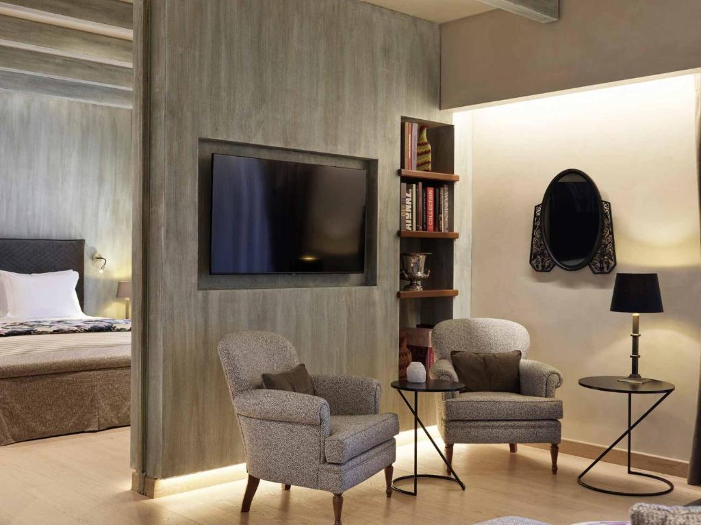 a bedroom with a bed and two chairs and a television at Semeli Estate Suites in Koútsion