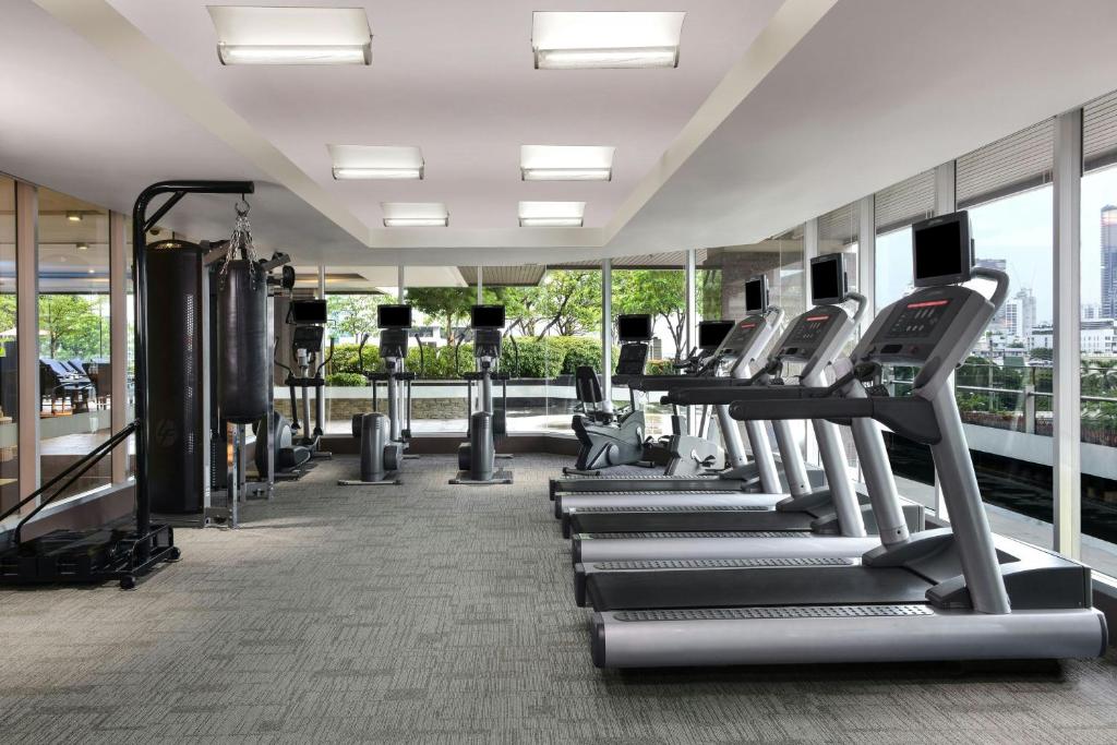 A bright fitness room with treadmills, cardio machines and strength equipment beside windows.