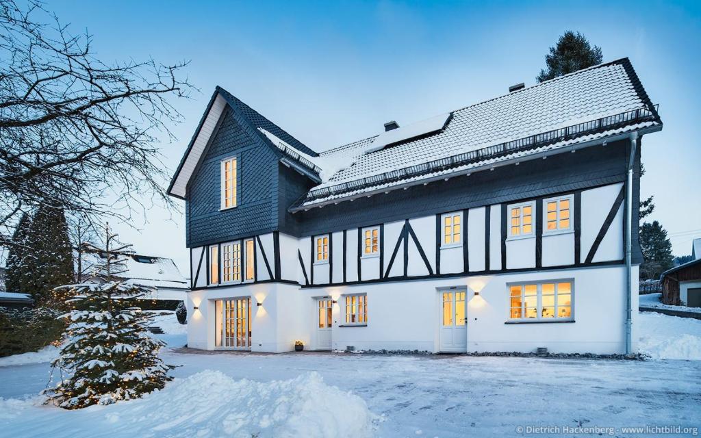 a white house with a black roof in the snow at Fachwerkhaus Eiben in Kirchhundem