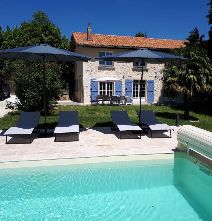 a pool with chairs and umbrellas next to a house at Les Côtes - Charming holiday home with heated swimming pool in Palluaud