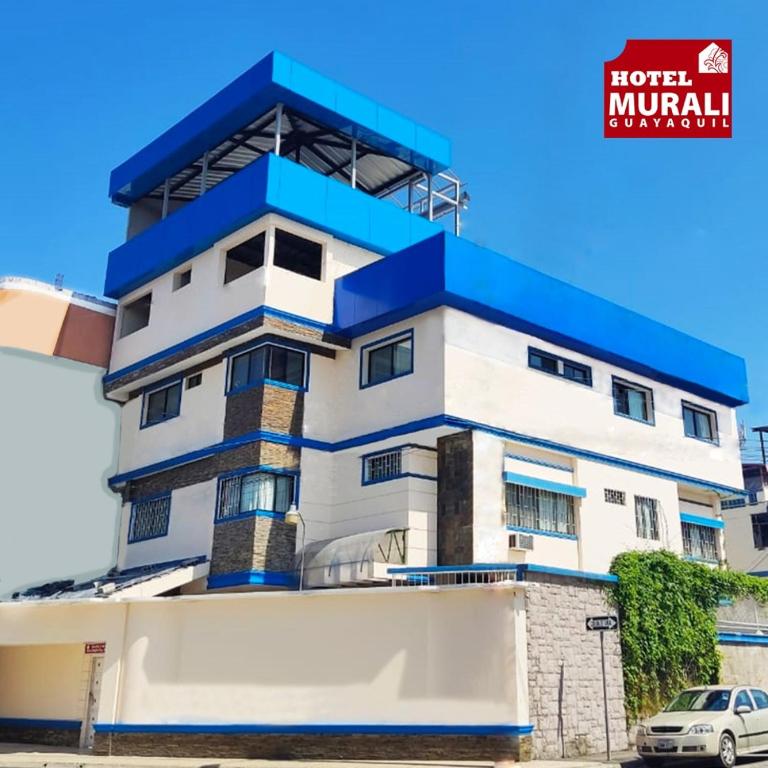 a white and blue building with a car in front at Hotel Murali - Cerca del Aeropuerto de Guayaquil in Guayaquil
