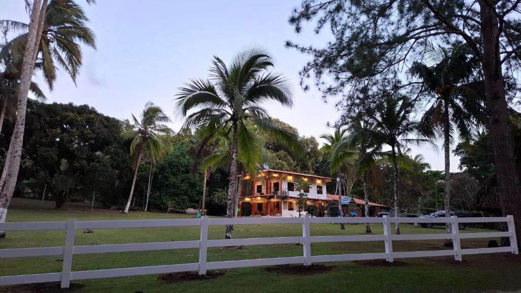a house behind a white fence with palm trees at Finca Agroturística La Amistad in Churuquita Grande