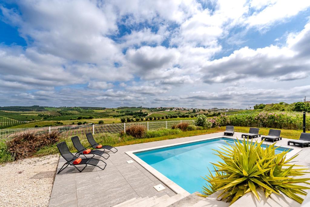 a swimming pool with chairs and a view of the countryside at Villa Adão Lobo in Cadaval