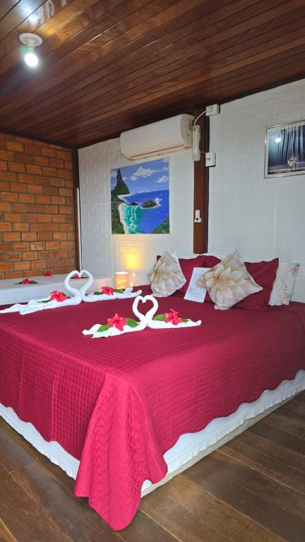 a large bed with a red bedspread with two roses on it at Pousada Capim Açu in Fernando de Noronha