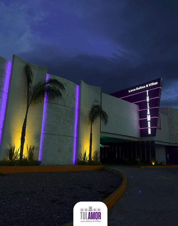 a building with palm trees in front of a building with purple lights at Tulamor Love Suites & Villas in San Lorenzo