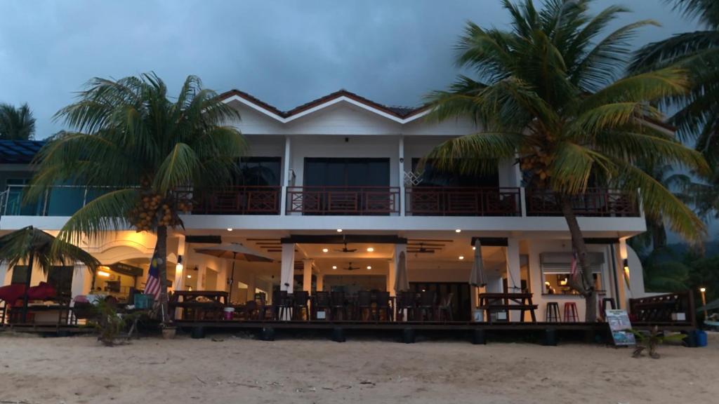 a building on the beach with palm trees in front at Juara Mutiara Resort in Tioman Island