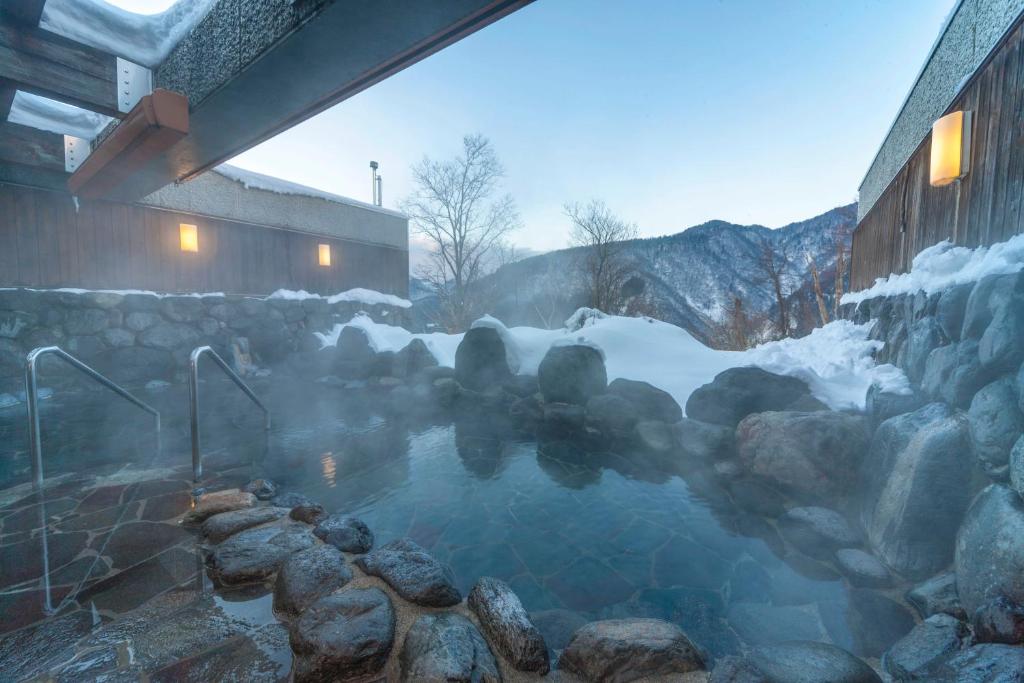 a hot tub with snow and rocks in front of a building at Hotel Morinokaze Tateyama‎ in Toyama