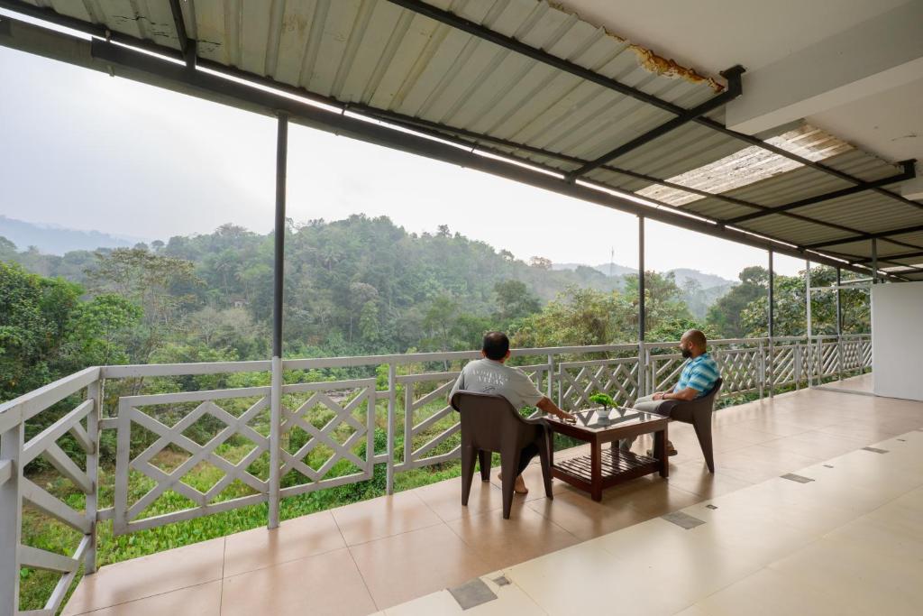 two people sitting at a table on a balcony with a view at Skybz Resort - Mankulam in Viripara