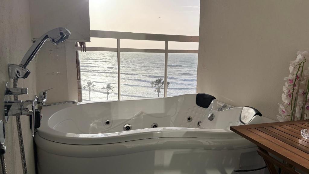 a white bath tub in a bathroom with a window at קו המים - Waterline סוויטות עם גקוזי הכי קרוב לים in Netanya