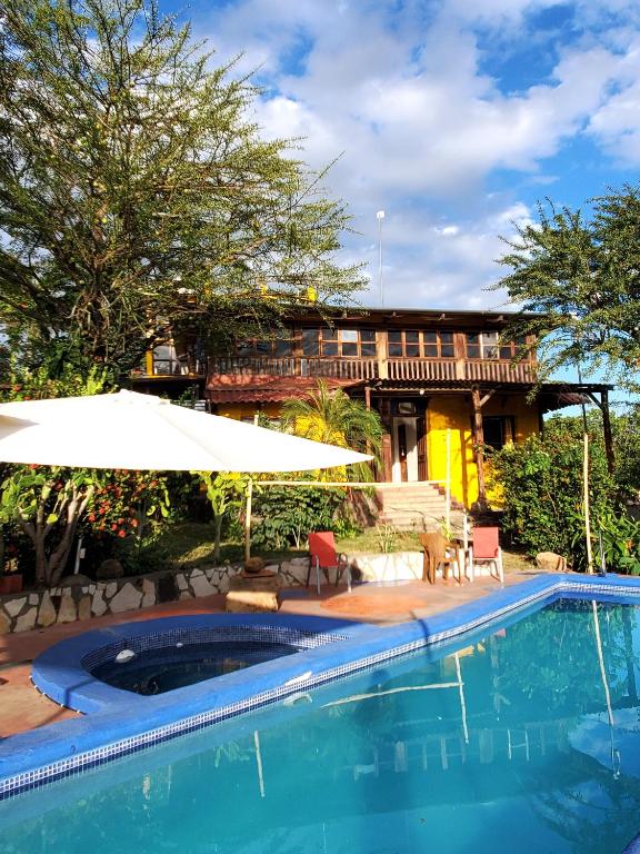 a swimming pool with an umbrella and a house at Yellow Submarine Hostal in Poneloya