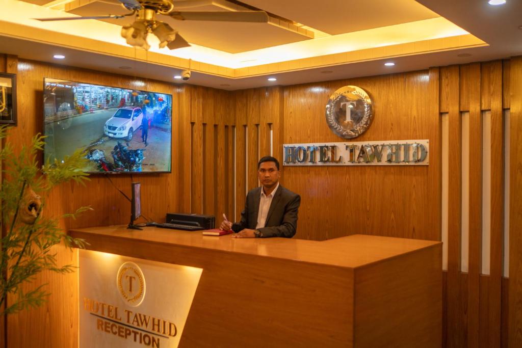 a man is sitting at a reception desk at Hotel Tawhid in Rangpur